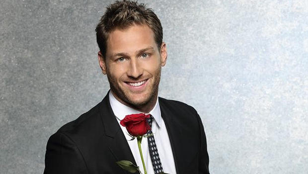 Smiling man in suit holding red rose.